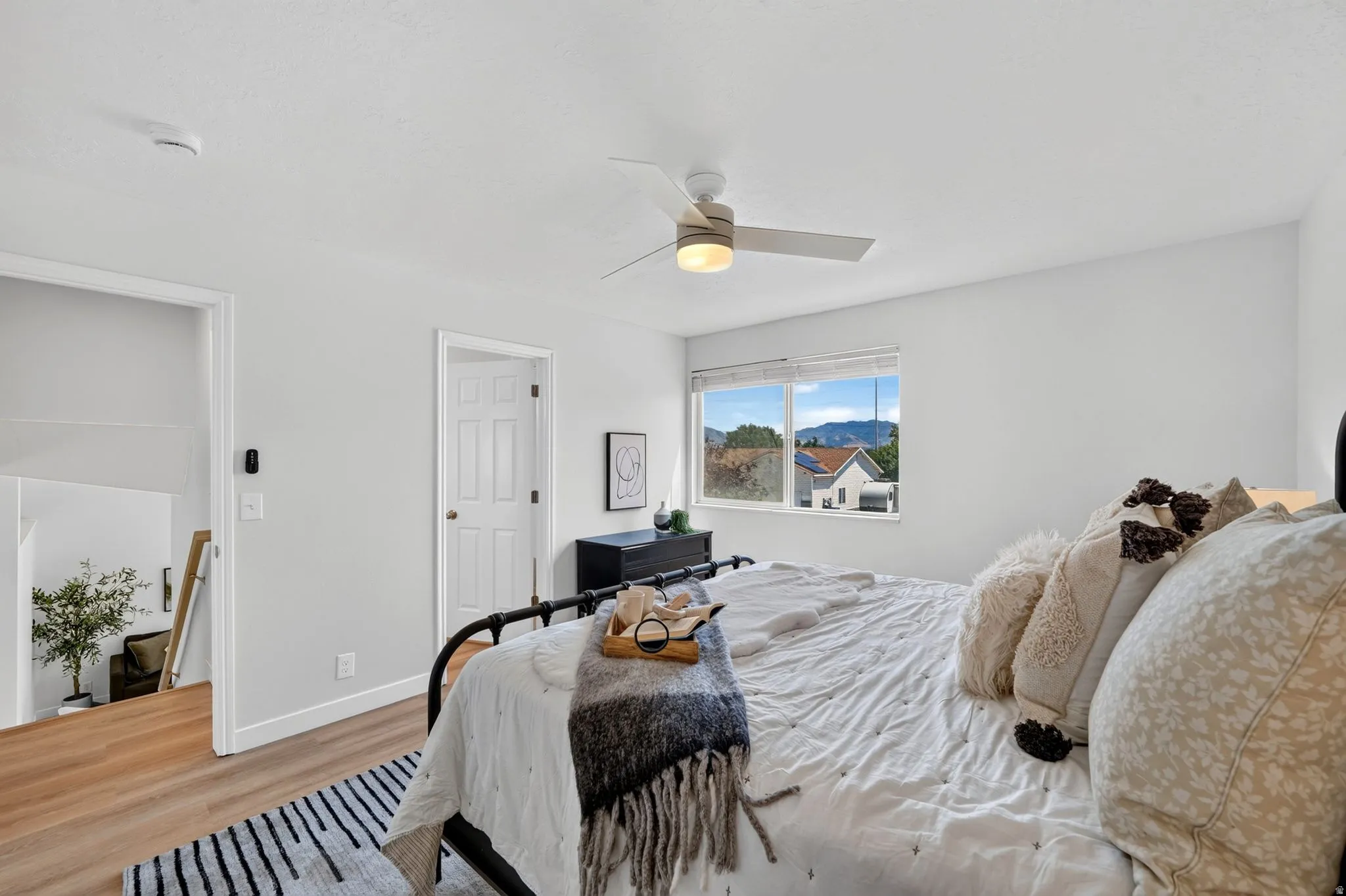 Bright bedroom featuring a window with a mountain backdrop, a ceiling fan with integrated lighting, wood-finish flooring, and white walls