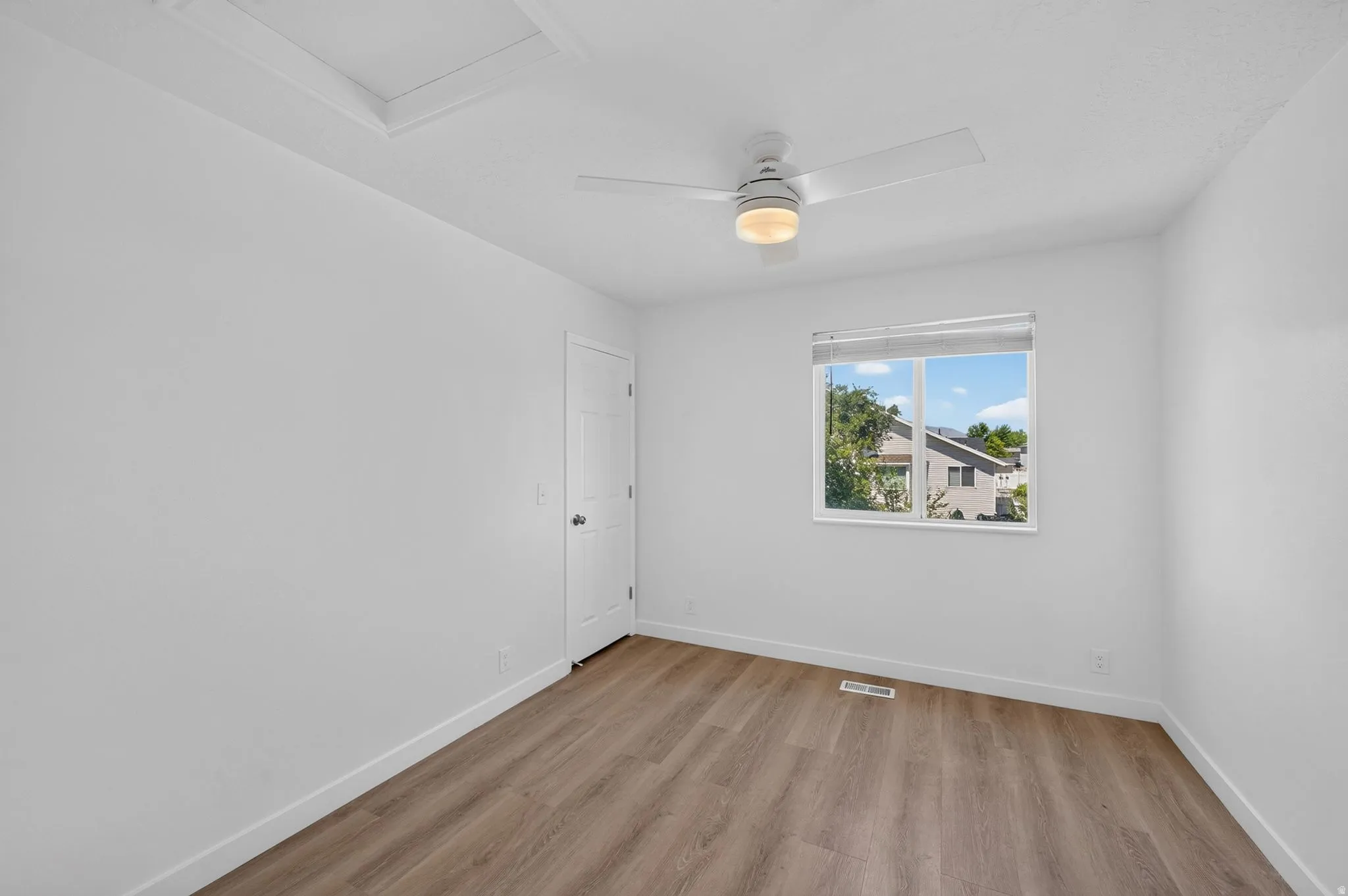 Bright room featuring wood-finish flooring, a contemporary ceiling fan with integrated lighting, a window with a white frame, and white baseboards