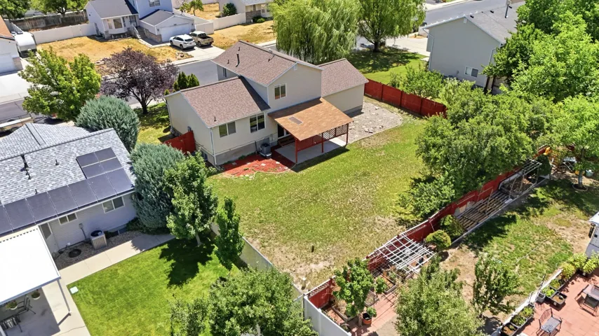 Expansive rear yard featuring a large patio cover, mature trees, and a red perimeter fence