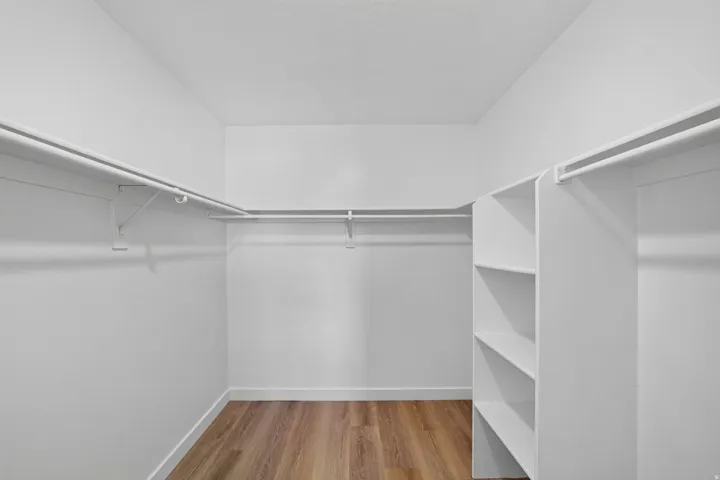 Walk-in closet featuring wood-finish flooring, white walls, built-in shelving, and multiple clothing rods