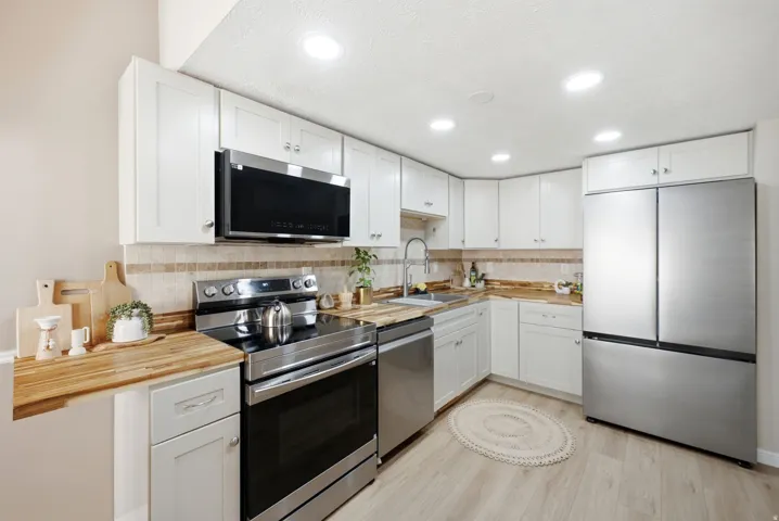 Kitchen featuring white cabinetry, stainless steel appliances, wood-finish countertops, tile backsplash, and recessed lighting