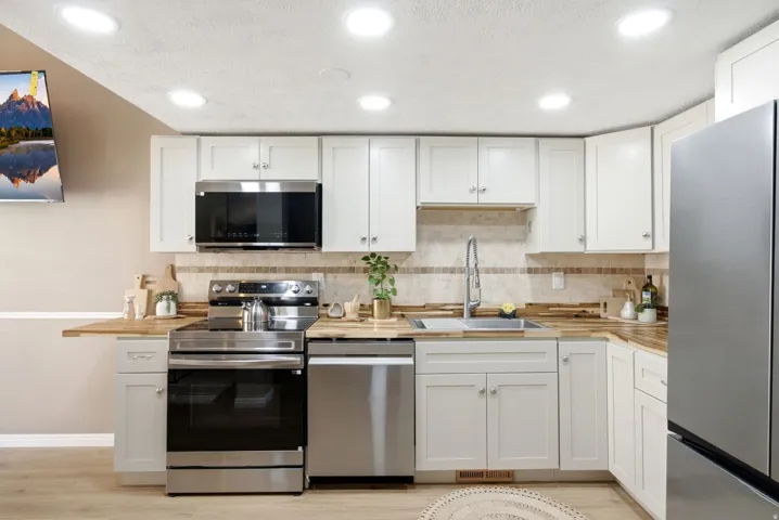 Kitchen featuring white cabinetry, wood-finish countertops, stainless steel appliances, a tile backsplash, and recessed lighting