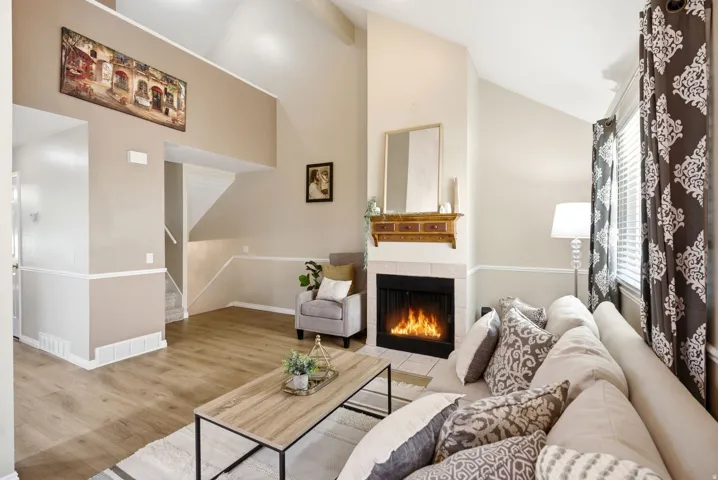 Vaulted ceilings enhance the living space featuring wood-finish flooring, a fireplace with a tile surround, and a decorative mantel