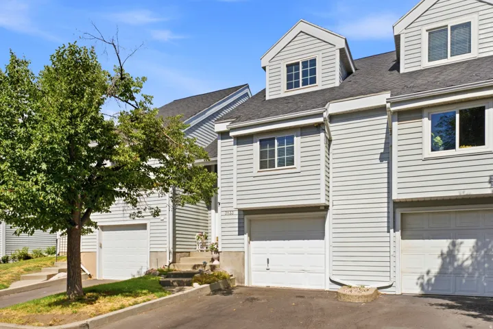 Multi-level townhome featuring light gray horizontal siding, an attached garage, and multiple dormer windows