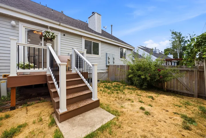 Exterior siding, composite deck with white railings and black balusters, sliding glass door, mature landscaping, and wood perimeter fencing