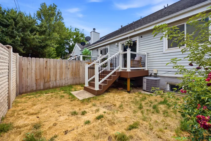Rear exterior featuring a composite deck with white railings, direct access to the interior via a sliding glass door, and a wood privacy fence