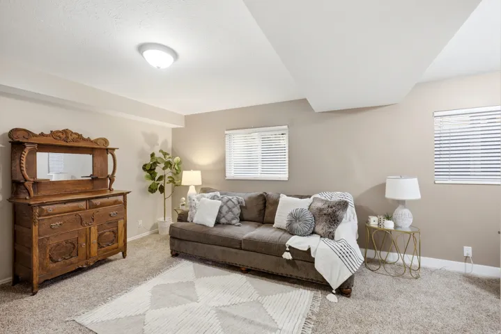 Large living room featuring carpet flooring, two windows with blinds, and white baseboards
