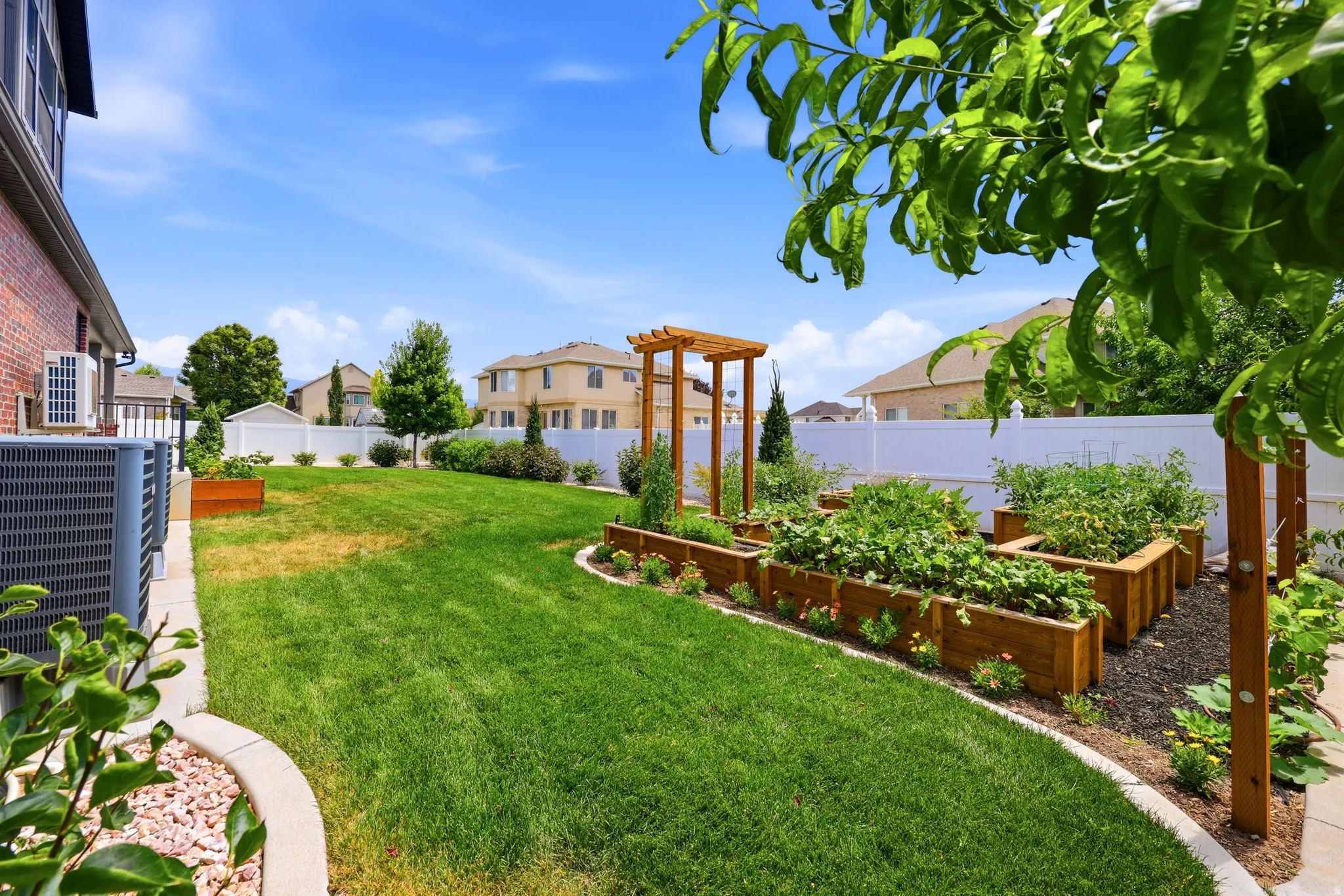 Expansive backyard featuring multiple raised garden beds, a pergola, a manicured lawn, and a white privacy fence