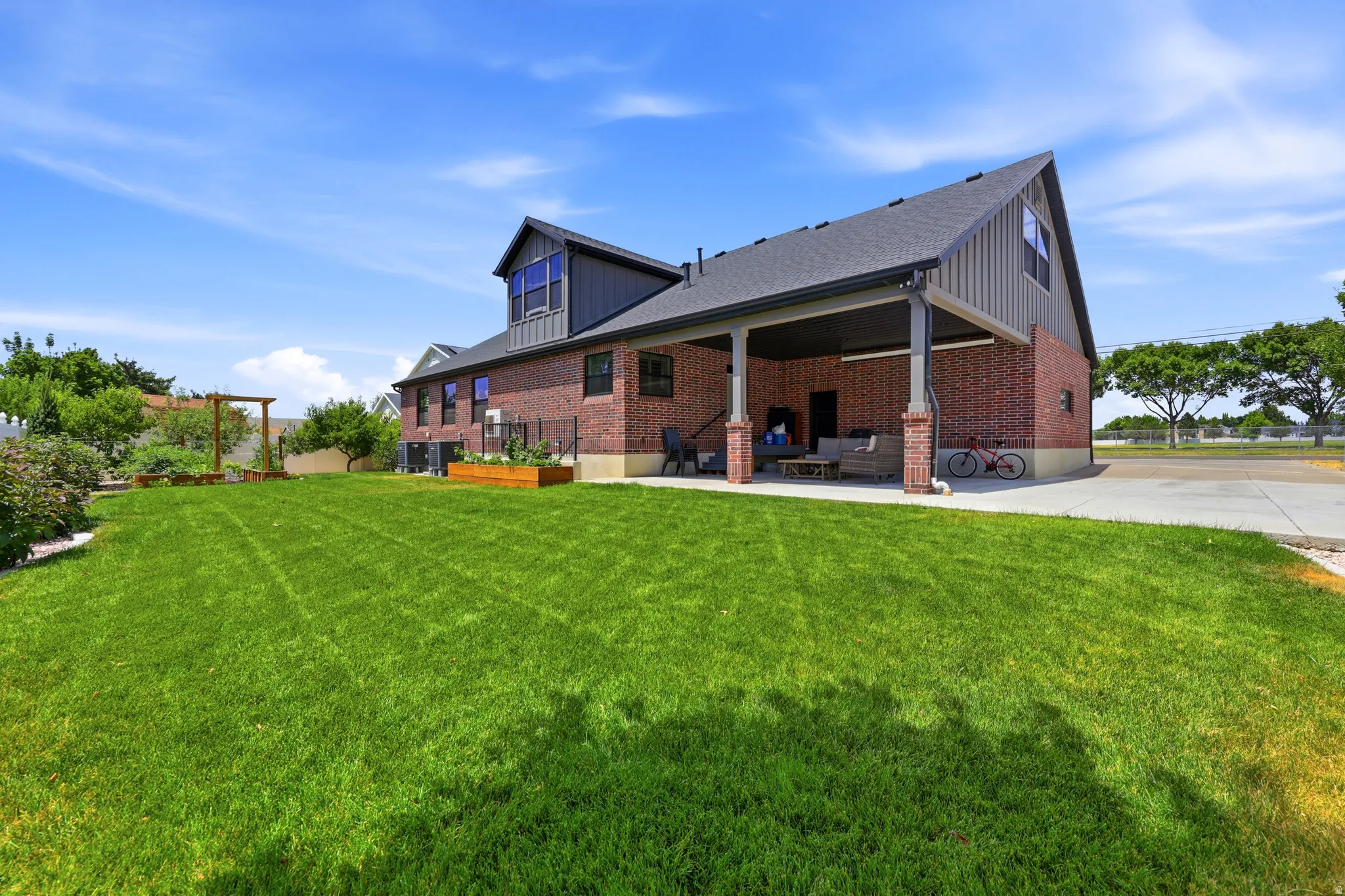 Expansive green lawn with a covered patio, brick exterior, and a dormer window