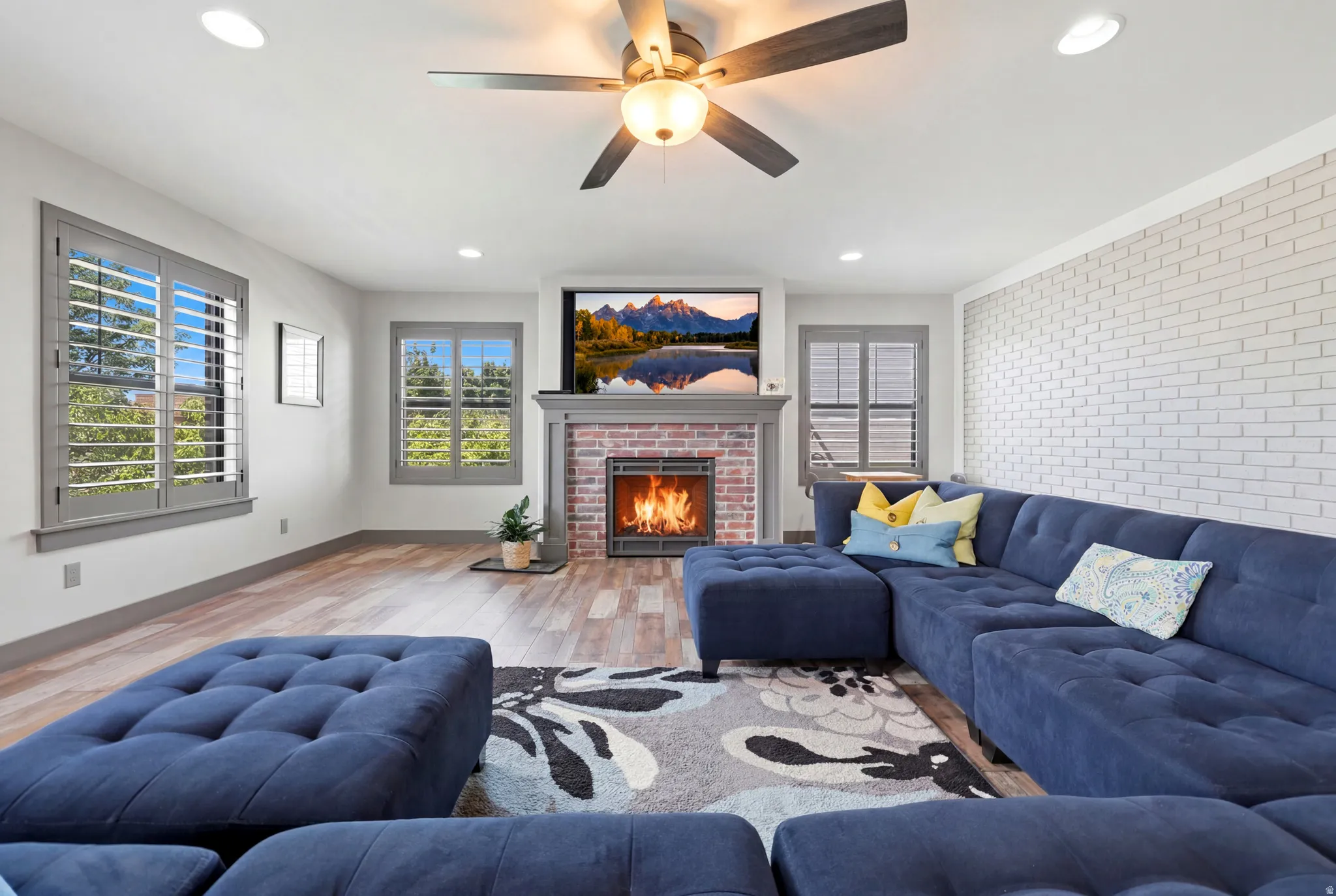 Living area featuring wood-finish flooring, a brick fireplace with a mantel, recessed lighting, and a ceiling fan with integrated lighting