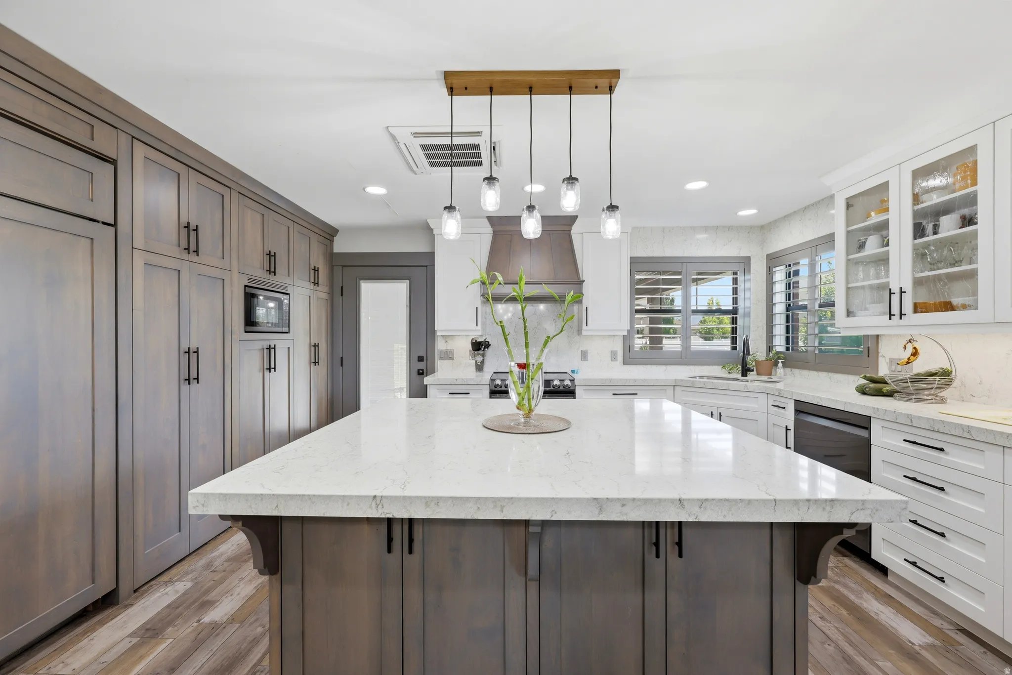 Spacious kitchen featuring a large central island with a light-toned countertop, wood-finish flooring, full-height cabinetry, and a combination of white and natural wood-tone finishes
