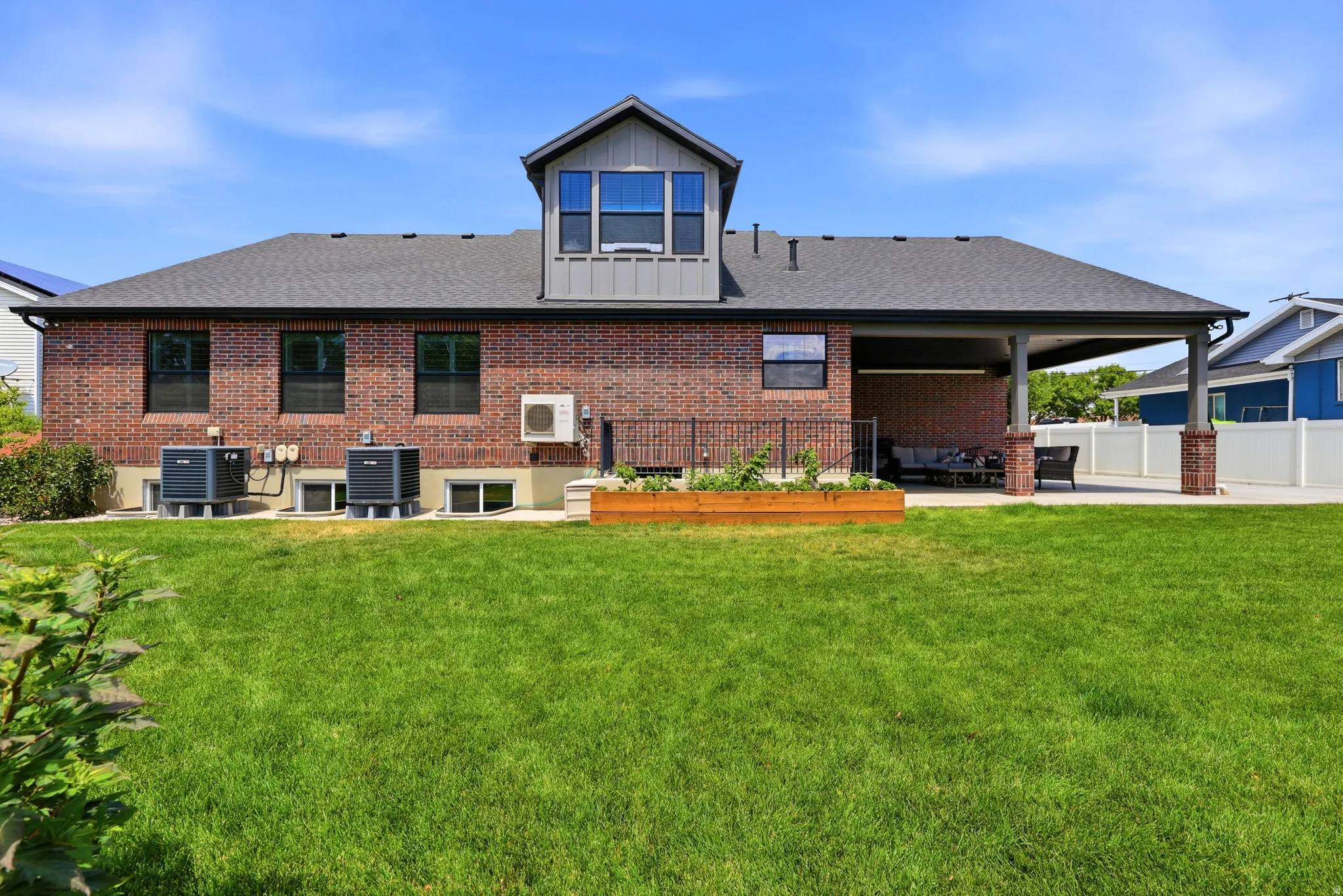 Brick exterior featuring a covered patio, dormer window, and multiple window wells