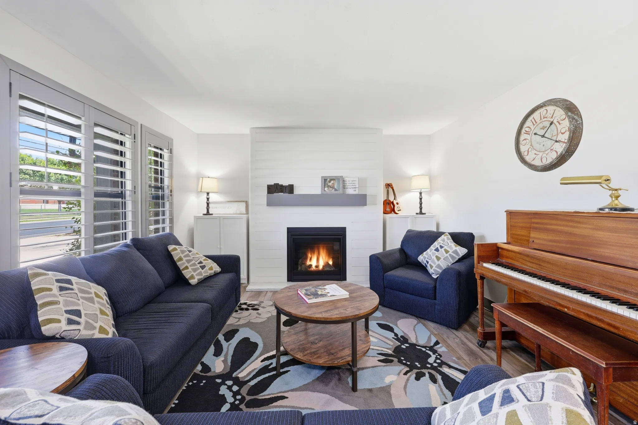 Living area featuring a modern fireplace, plantation shutters, wood-finish flooring, and white walls