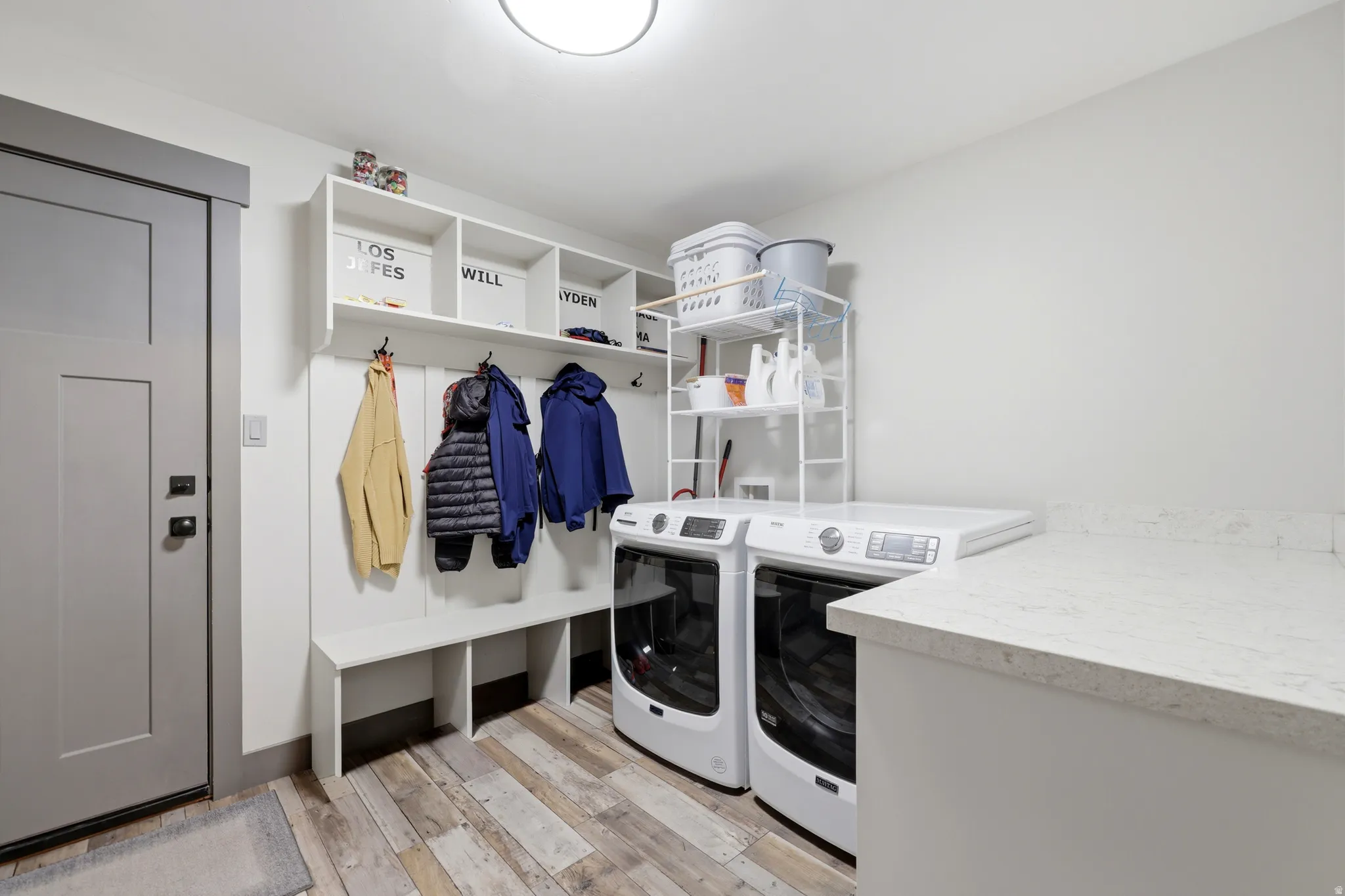 Dedicated laundry area featuring wood-finish flooring, a built-in bench with storage cubbies, and overhead shelving