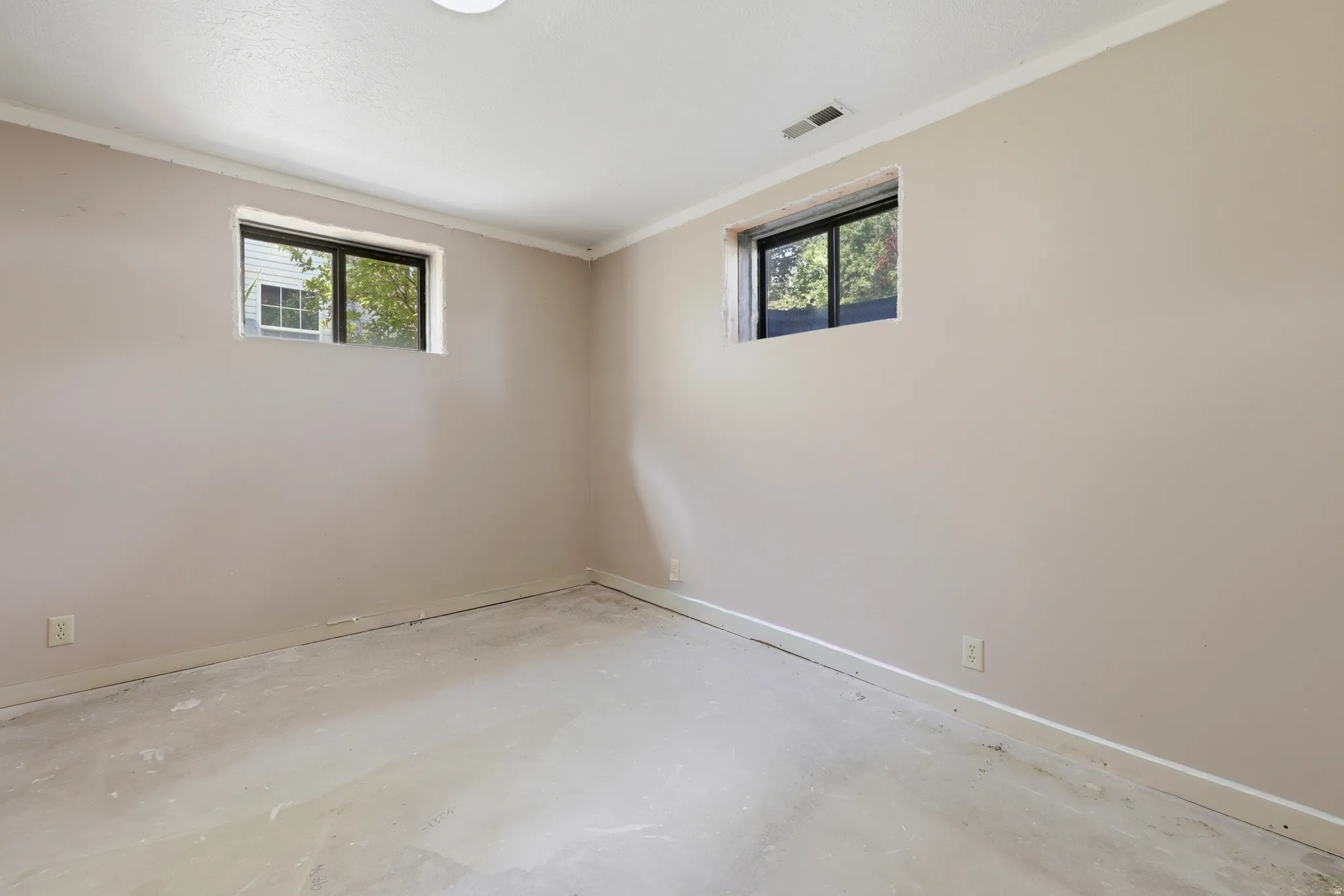 Unfinished room featuring two windows with dark frames, light beige walls, a white ceiling, and a concrete floor