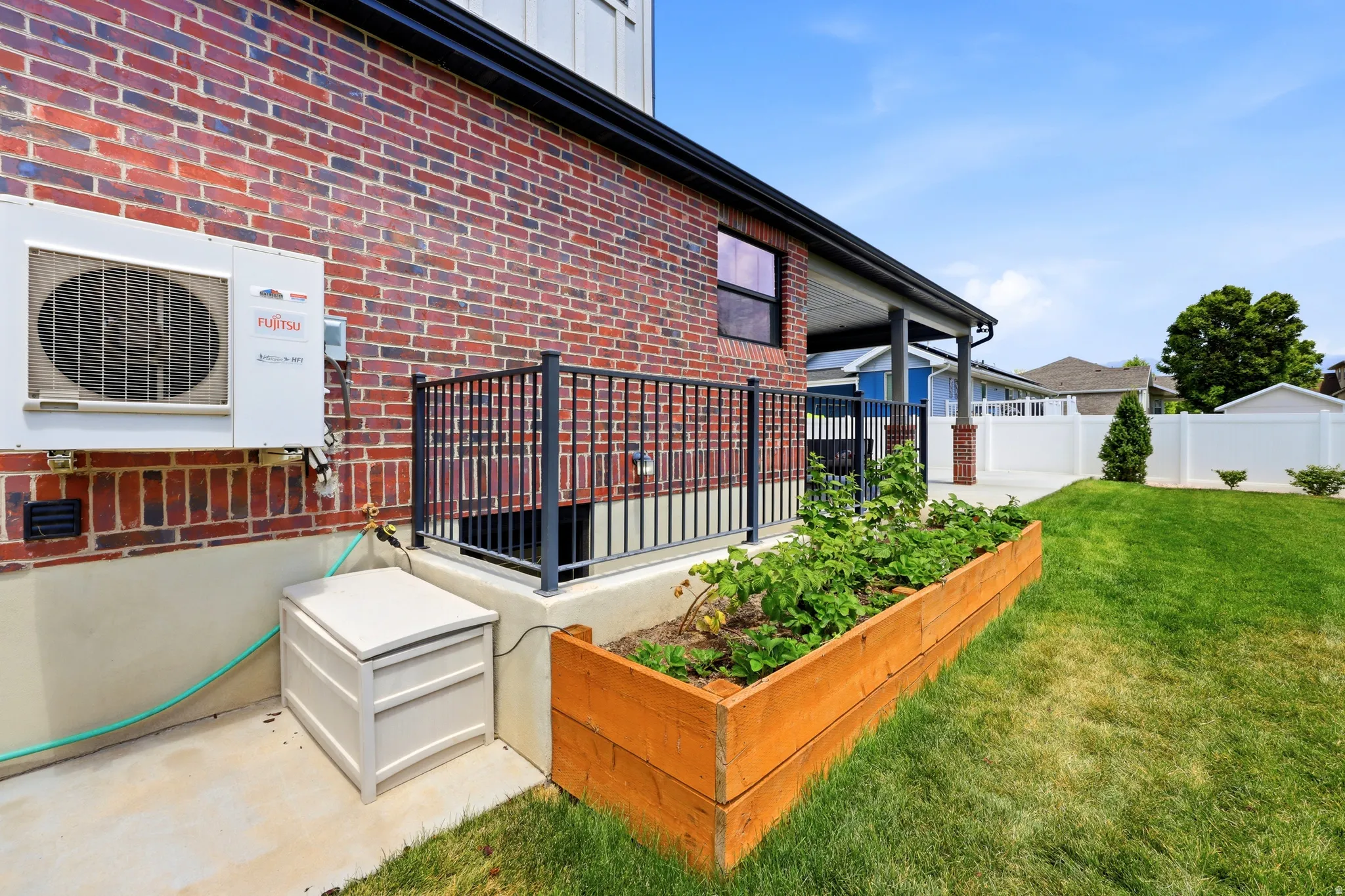Backyard featuring a red brick exterior, a covered patio, a raised garden bed, and a well-maintained lawn
