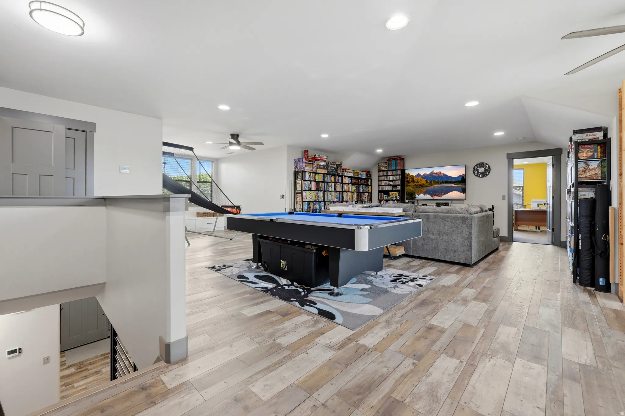Spacious open-concept room featuring wood-finish flooring, recessed lighting, ceiling fans, and a built-in shelving unit