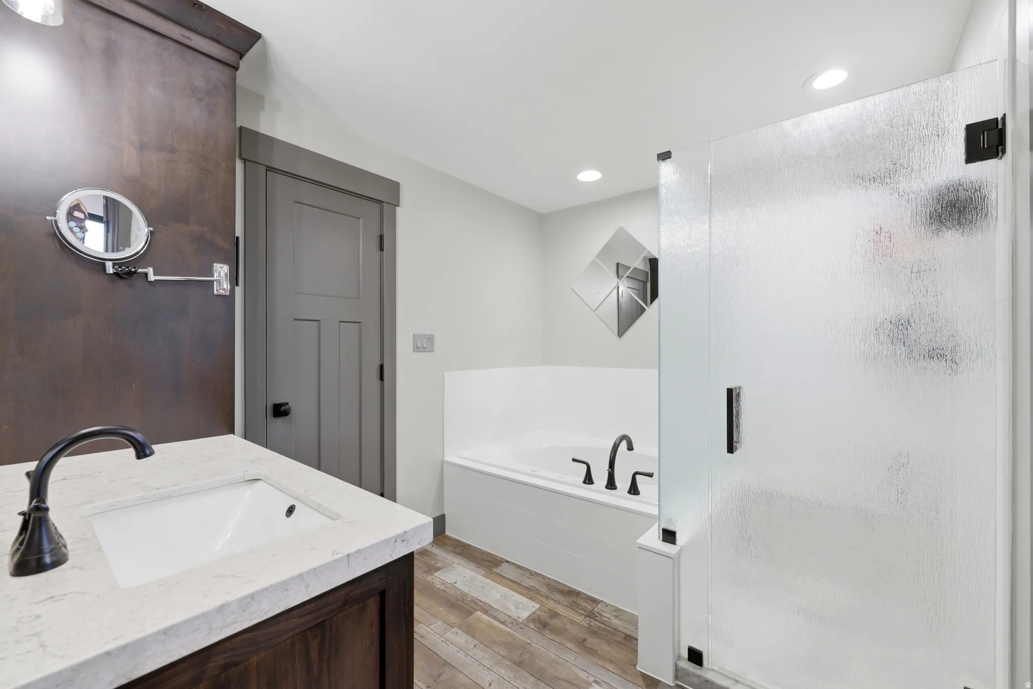 Bathroom featuring a white undermount sink with a dark bronze faucet, a white soaking tub with dark bronze fixtures, and a glass shower enclosure with a dark bronze handle