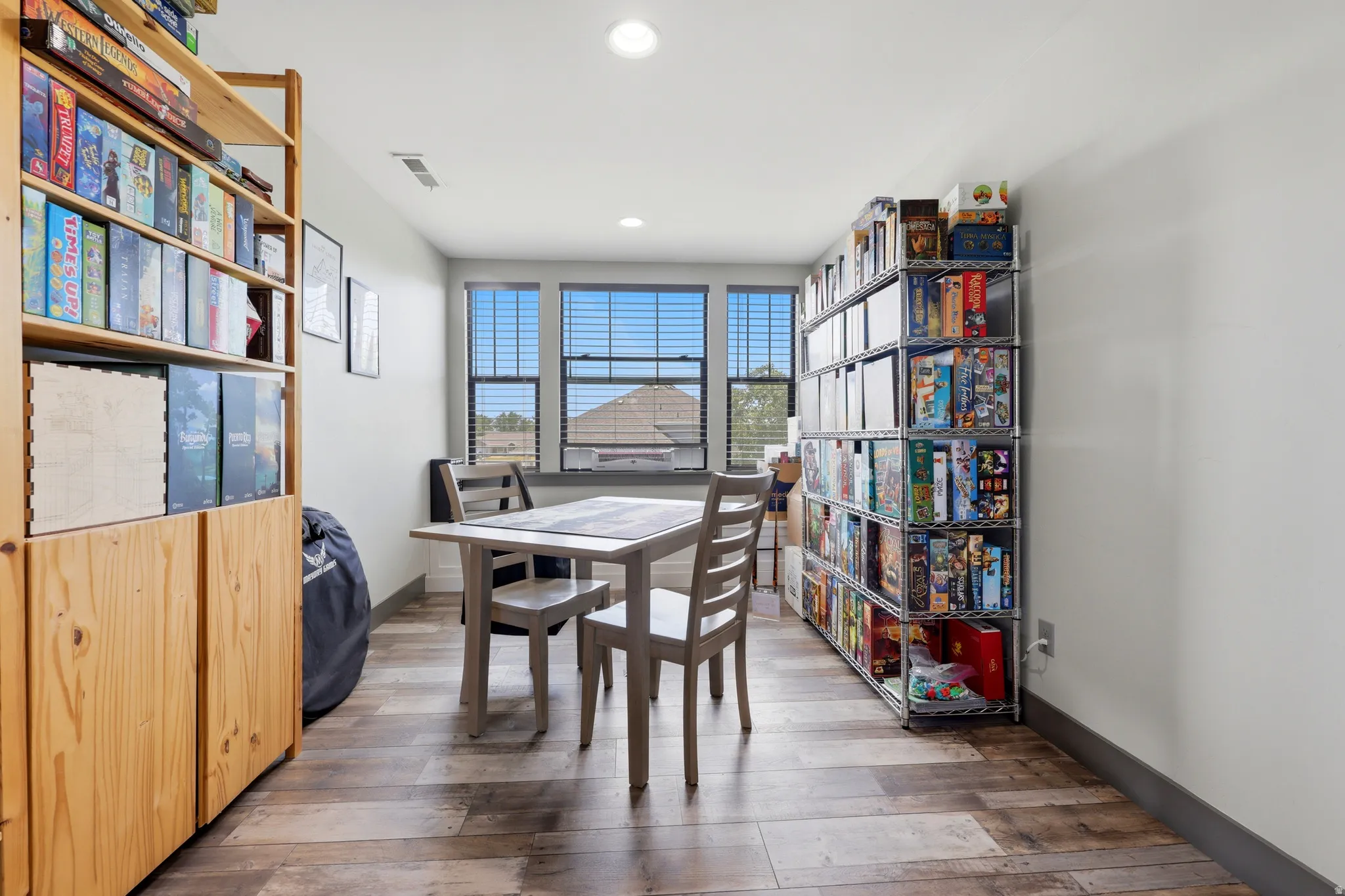 Bright room featuring three windows with blinds, wood-finish flooring, and recessed lighting