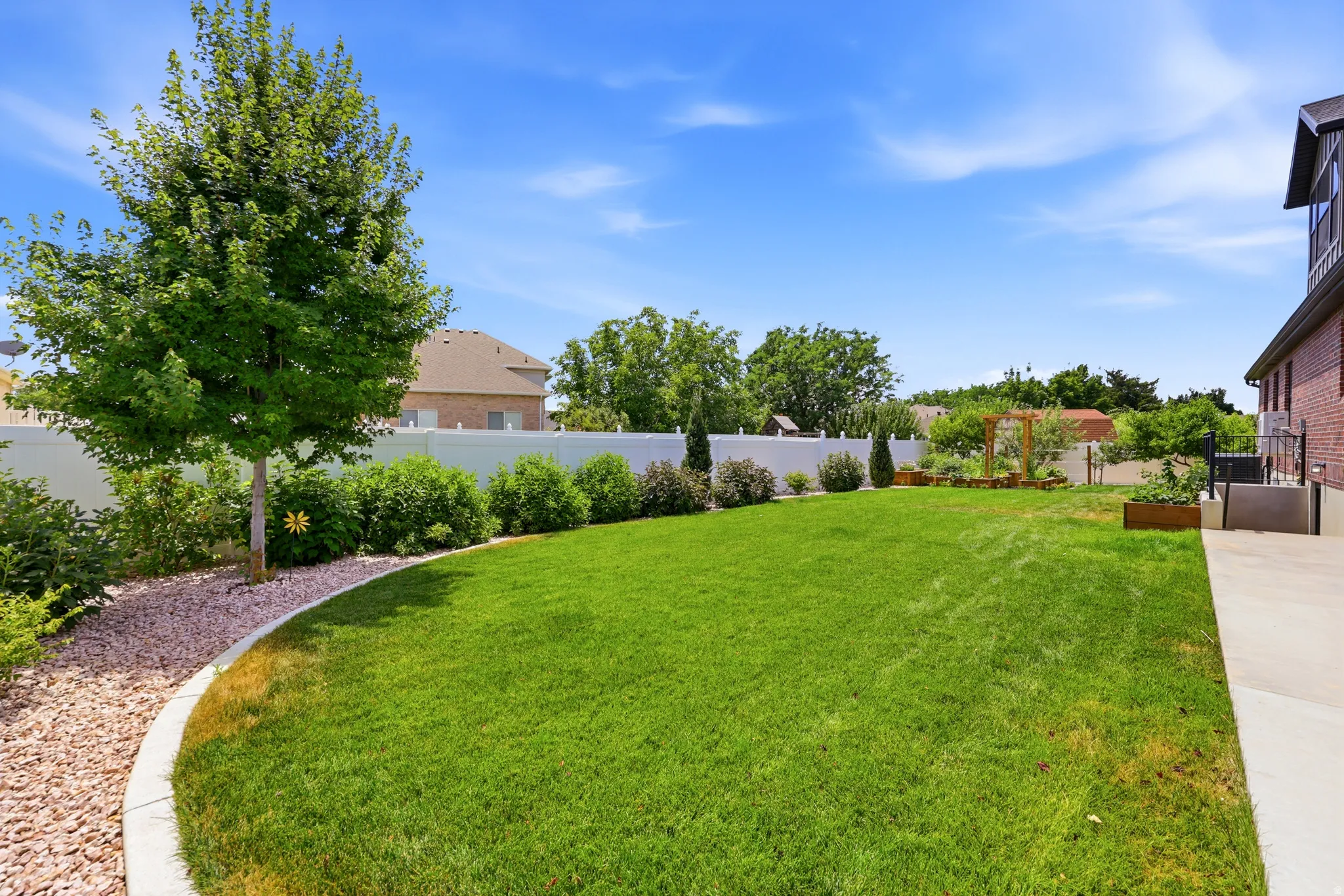 Expansive backyard featuring a lush lawn, mature trees, white privacy fencing, and a concrete patio
