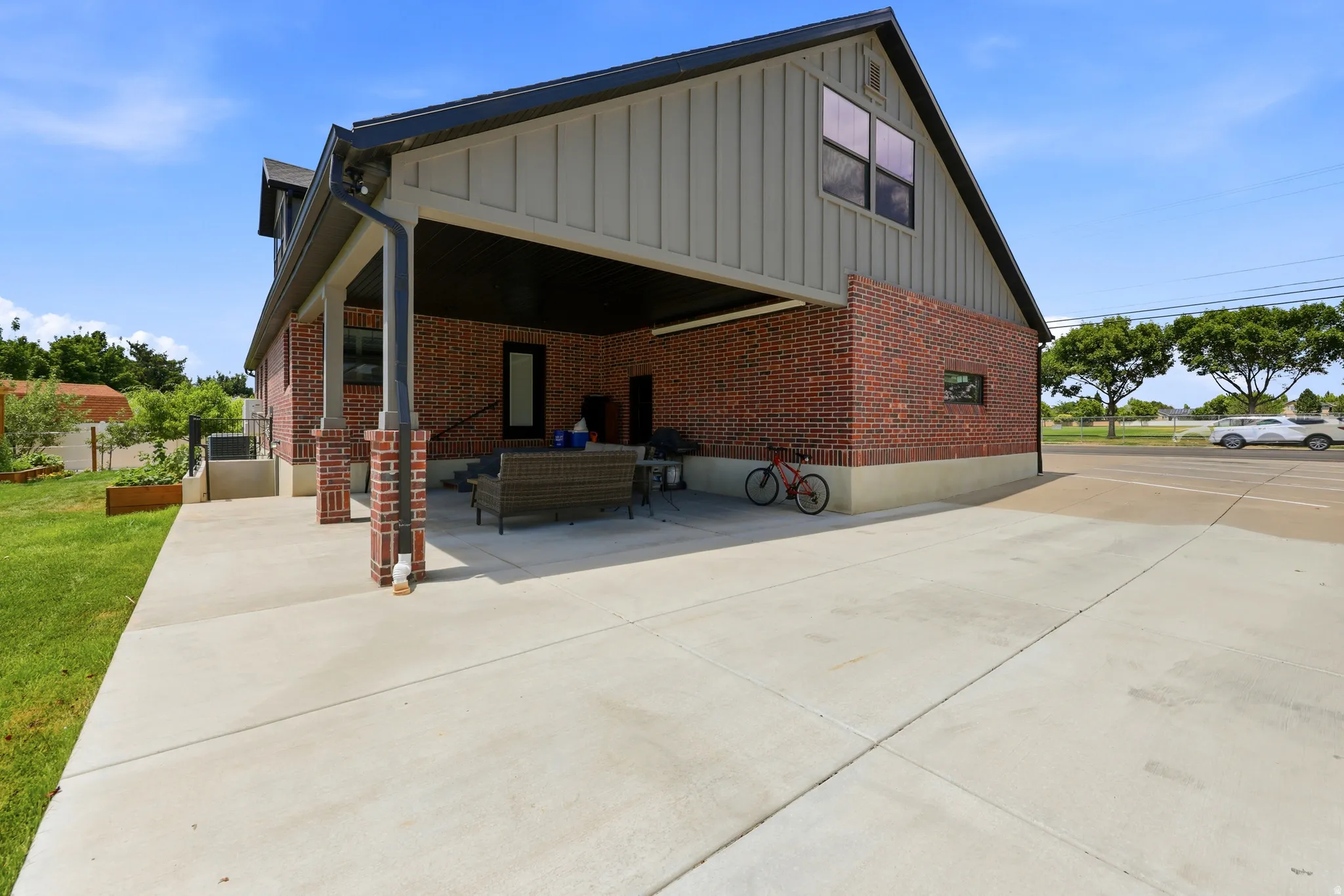 Exterior featuring brick and vertical siding, concrete driveway, covered patio area, and raised garden beds