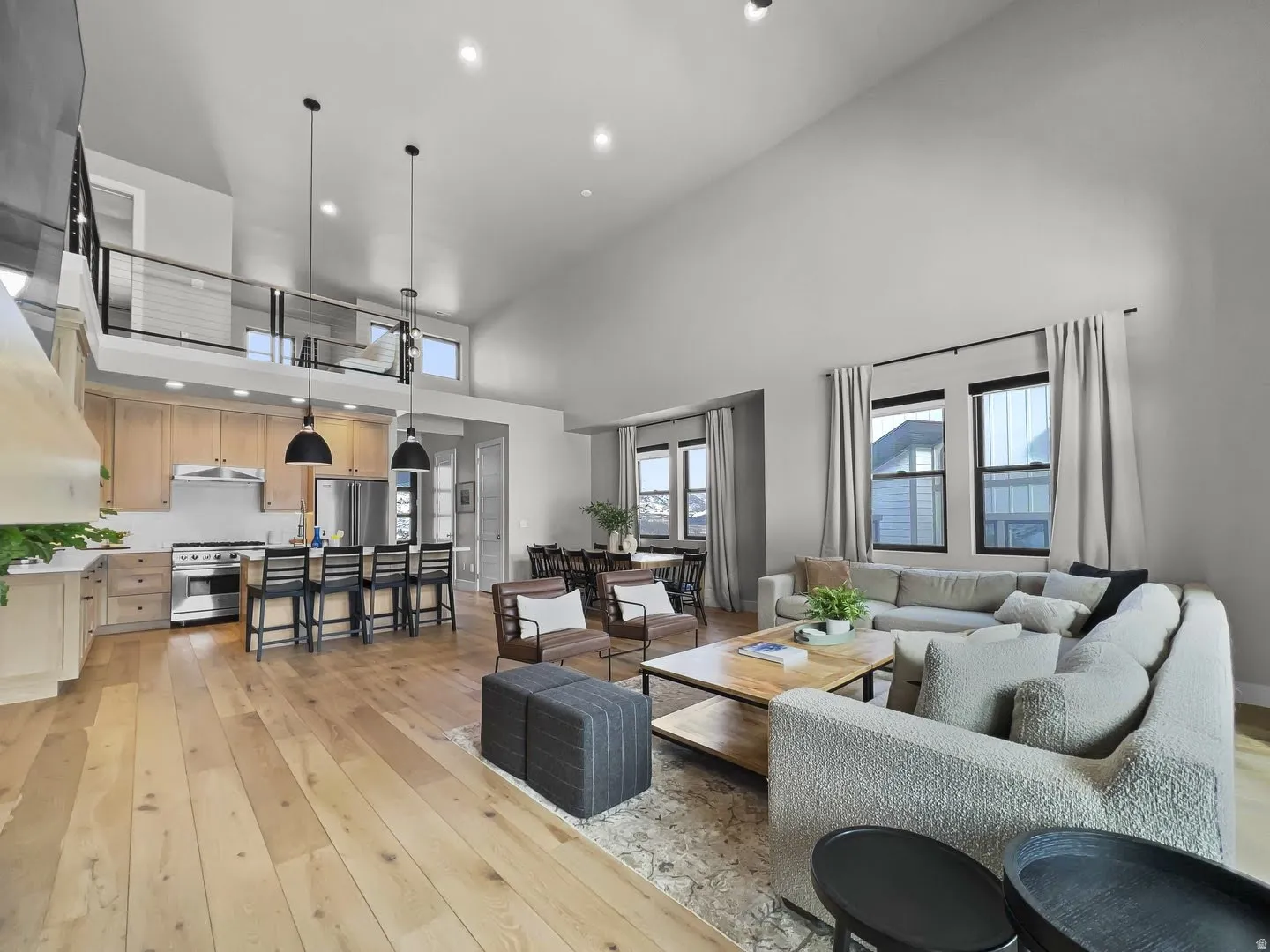 Open-concept living space featuring wood-finish flooring, a kitchen island with seating, stainless steel appliances, and a second-story interior balcony