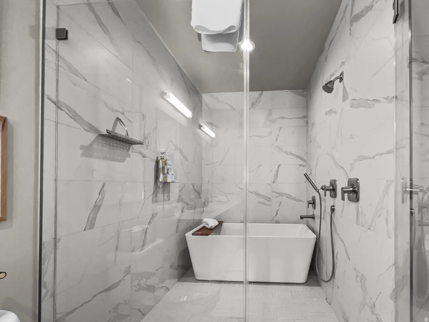 Walk-in shower enclosure featuring a freestanding soaking tub, full-height tile walls, a rain shower head, and a hand-held shower fixture