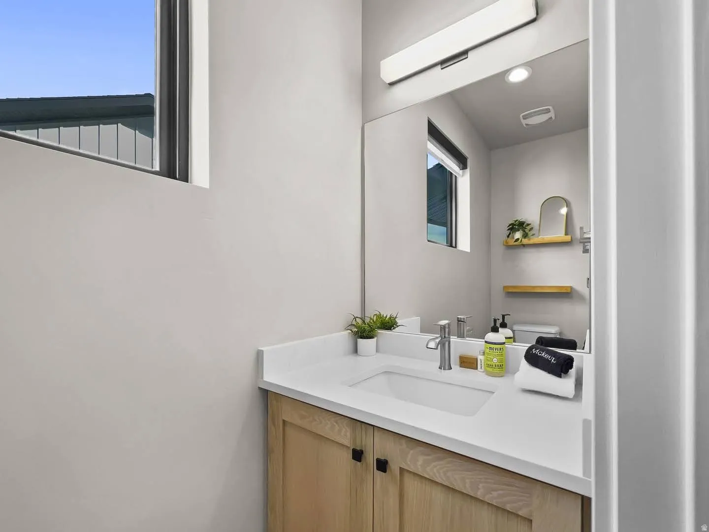 Modern vanity featuring light wood-finish cabinetry, a rectangular undermount sink, and a white countertop