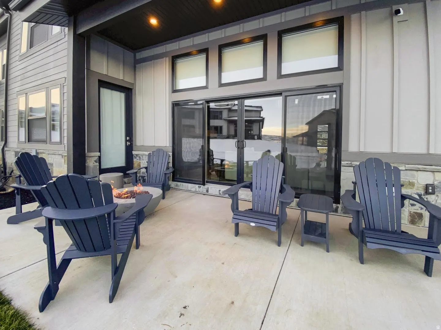 Expansive concrete patio with a modern fire pit, sliding glass doors, and recessed overhead lighting