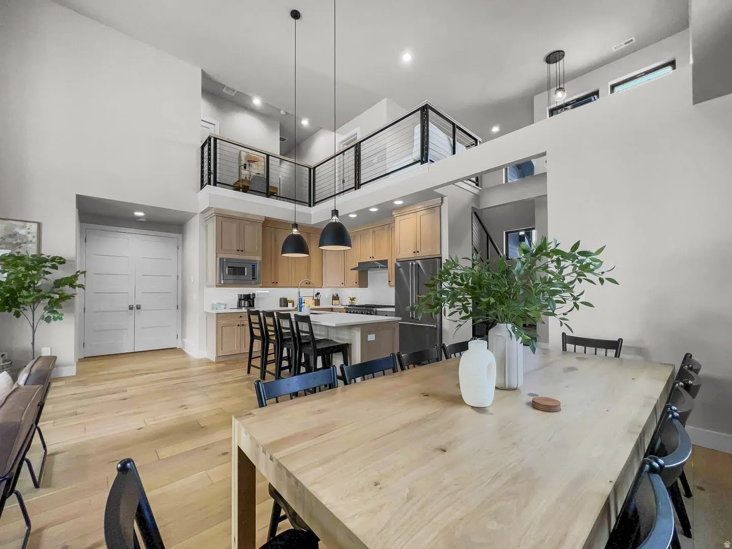 Open concept living space featuring a gourmet kitchen, light wood-finish flooring, and a second-story interior balcony with horizontal metal railings