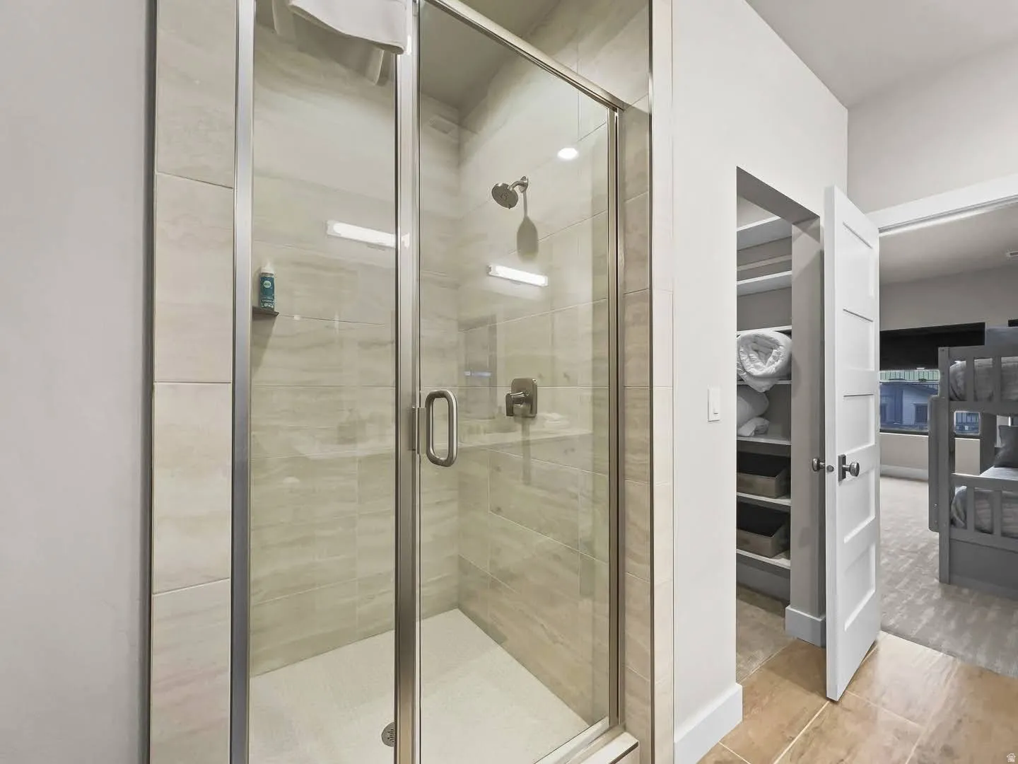 Glass-enclosed shower with tile surround and integrated shelving, featuring a mounted showerhead and a brushed nickel handle