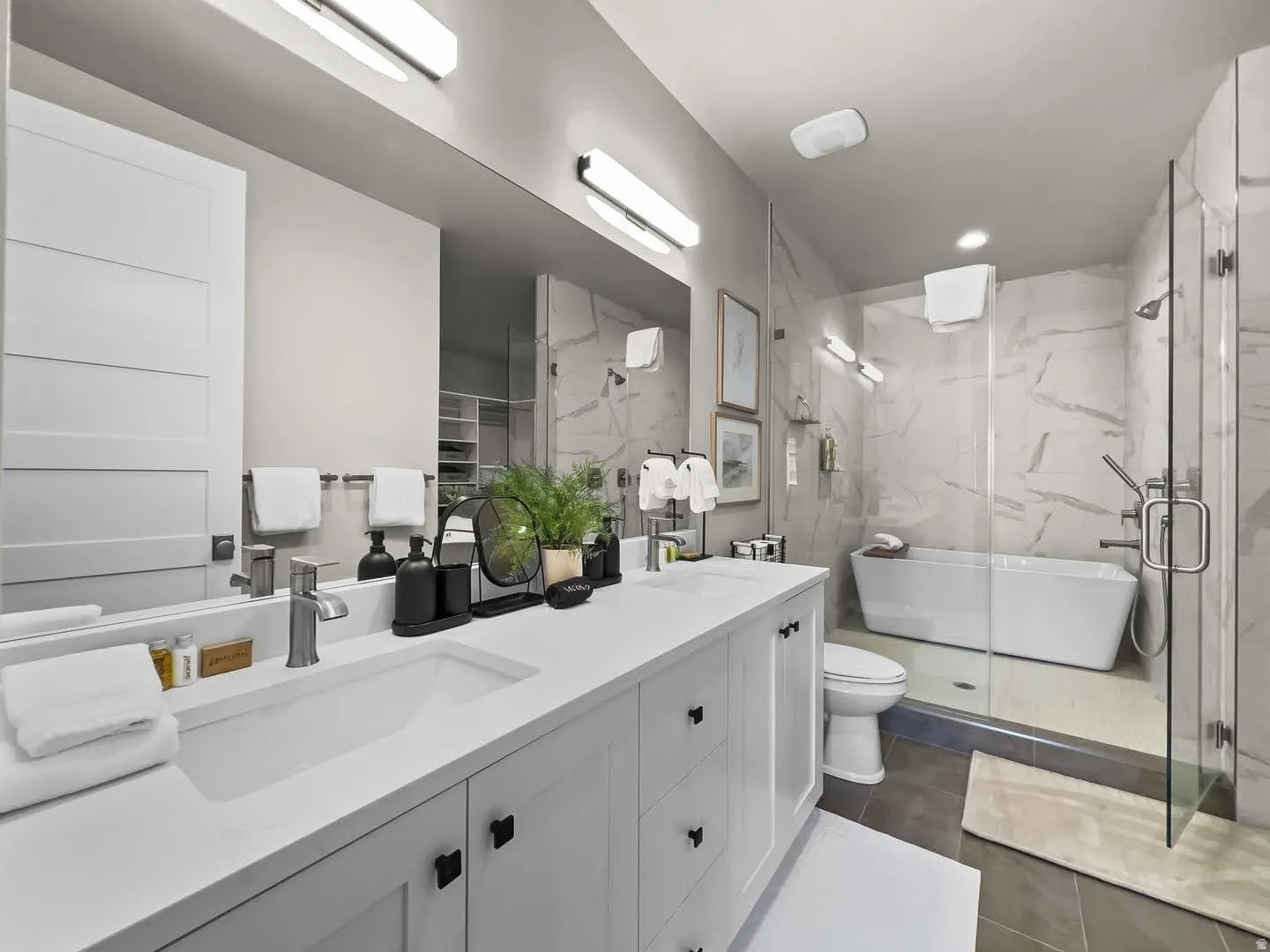 Contemporary bathroom featuring a double vanity with integrated sinks and black hardware, a freestanding soaking tub, a glass-enclosed shower, and large-format tile flooring