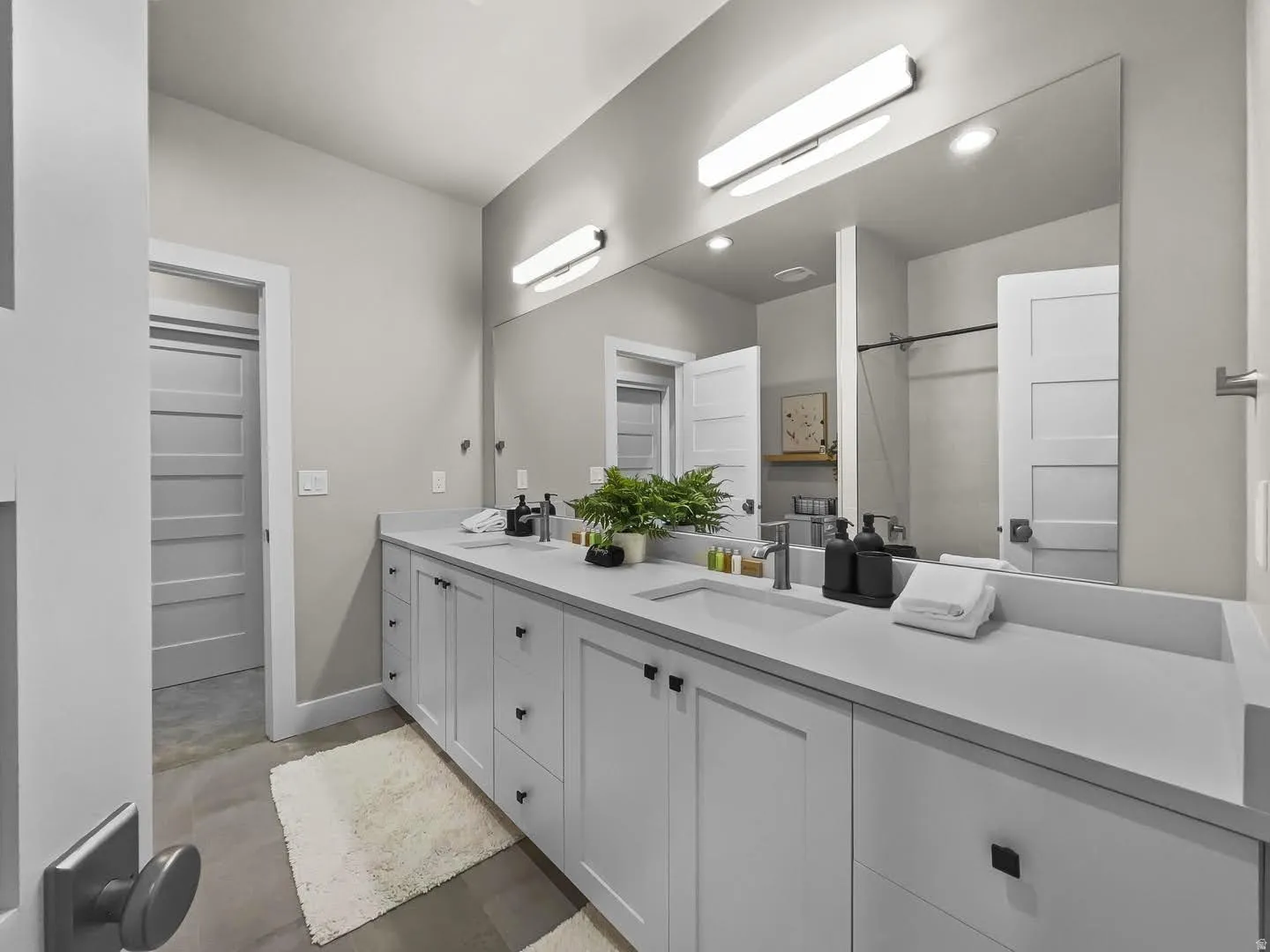 Spacious bathroom featuring a dual vanity with light gray cabinetry, integrated sinks, a large wall-mounted mirror, and matte black hardware