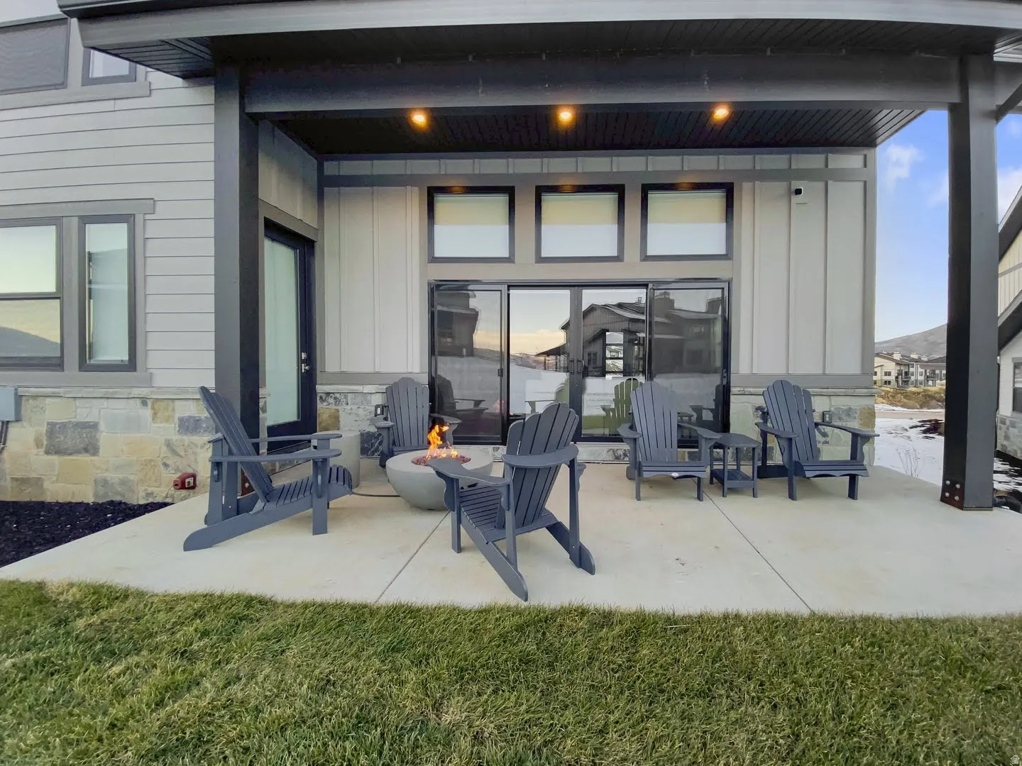 Covered concrete patio with a modern fire pit, large sliding glass doors, and a stone veneer foundation detail