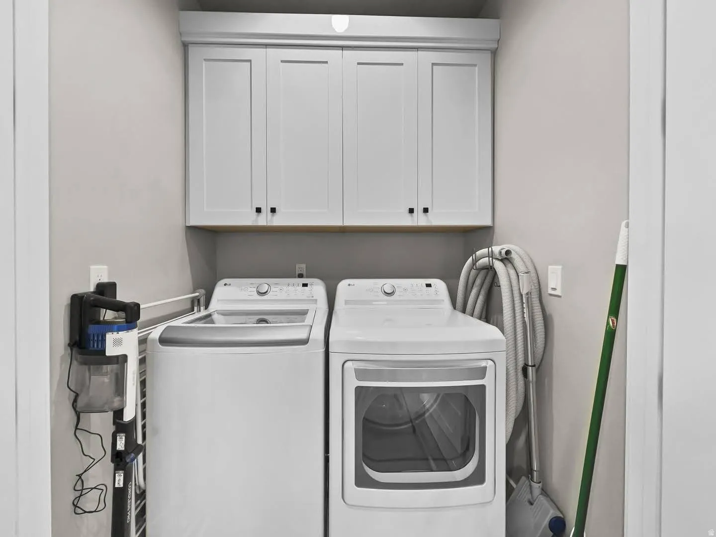 Dedicated laundry area featuring upper white shaker-style cabinetry with black hardware, a light wood-finish shelf, and neutral wall paint