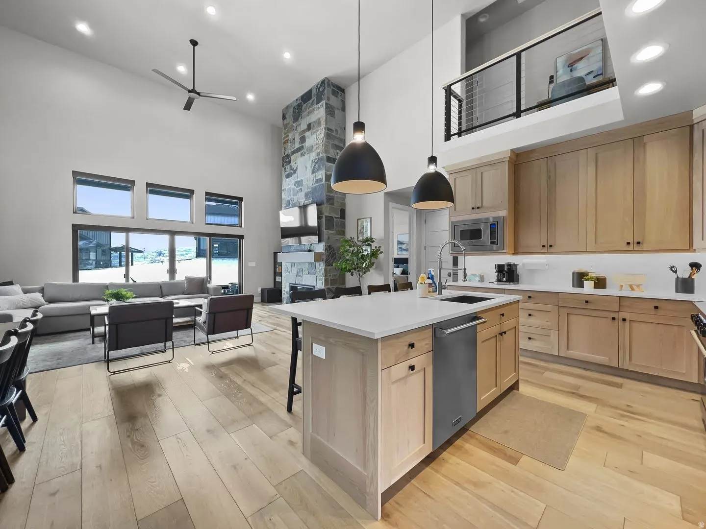 Open-concept living space featuring high ceilings, wood-finish flooring, a stone-clad fireplace, and a kitchen island with pendant lighting