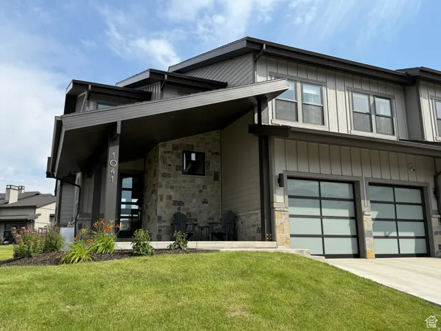 Modern exterior featuring vertical siding, stone accents, two contemporary garage doors, a covered entry, and landscaped plantings