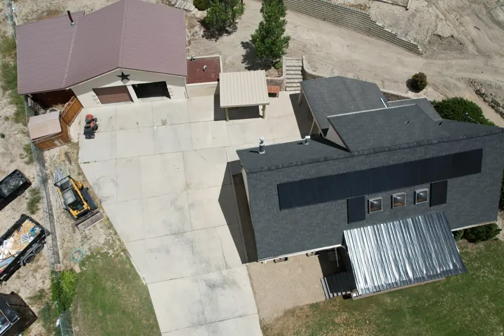 Main residence featuring a dark shingle roof with integrated solar panels and a corrugated metal awning