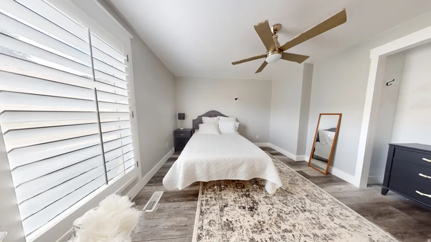 Bedroom featuring wood-finish flooring, plantation shutters, and a ceiling fan with integrated lighting
