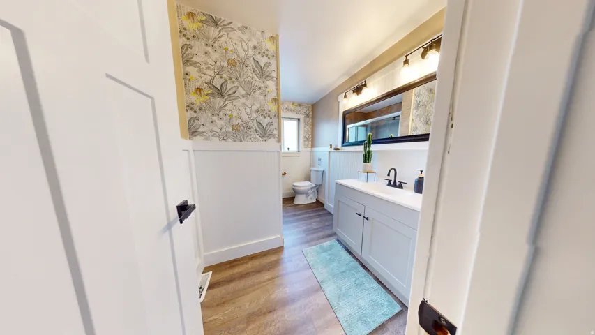 Bathroom featuring wood-finish flooring, white beadboard paneling, and botanical wallpaper