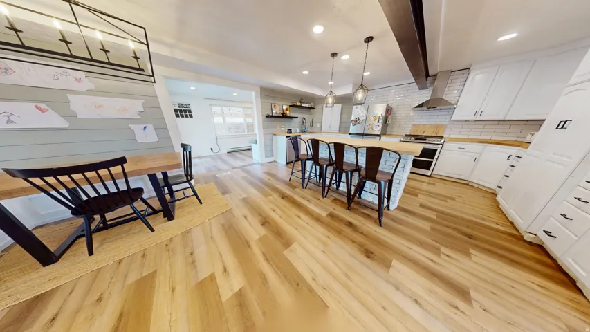 Spacious kitchen featuring wood-finish flooring, white cabinetry, wood countertops, a large center island with seating, and pendant lighting
