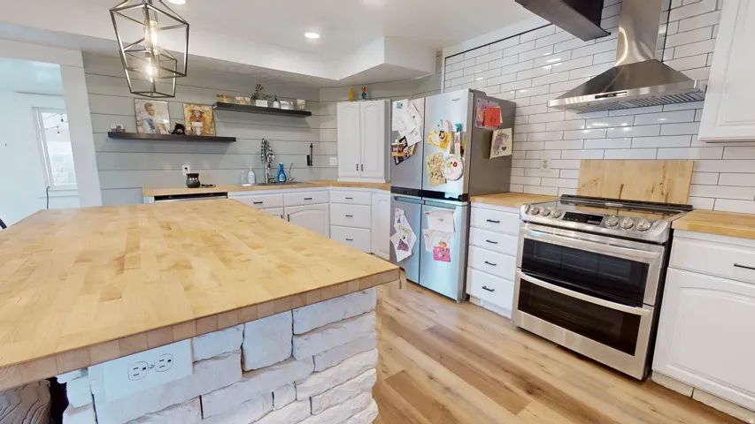 Gourmet kitchen featuring a large butcher block island, wood-finish flooring, white cabinetry, stainless steel appliances, and subway tile backsplash