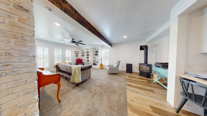Living space featuring a brick accent wall, wood-finish flooring, recessed lighting, and a dark wood ceiling beam