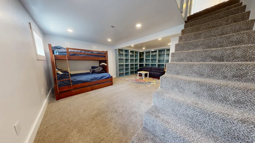 Carpeted staircase opening into a versatile recreation space featuring recessed lighting, extensive built-in shelving, and a window