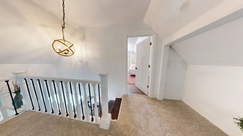 Carpeted landing featuring a white baluster and dark spindle railing, an open white paneled door, and a brass orb chandelier