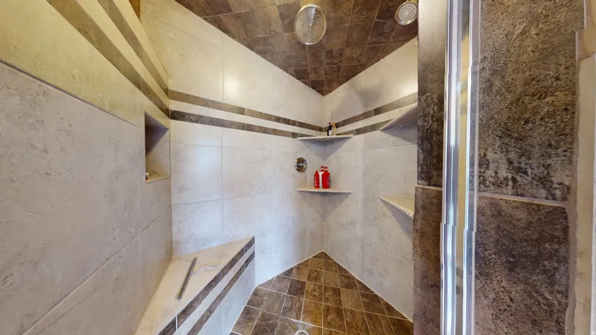 Walk-in shower featuring multiple shower heads, integrated corner shelving, built-in bench seating, and contrasting tile accents