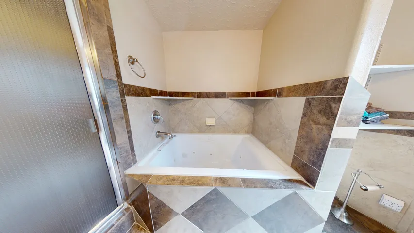 Built-in jetted tub surrounded by multi-tone tile with an integrated glass-enclosed shower