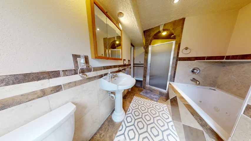 Full bathroom featuring a white pedestal sink, a wood-framed medicine cabinet, a tiled shower enclosure with a frosted glass door, and a corner soaking tub with jets