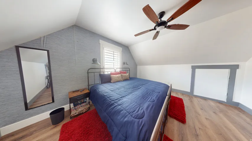 Attic bedroom featuring angled ceilings, wood-finish flooring, and a ceiling fan