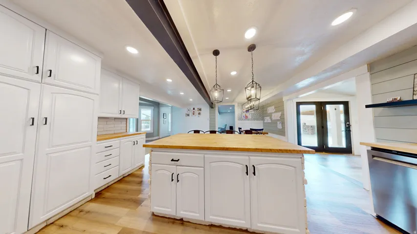 Open-concept kitchen featuring an expansive center island with butcher block countertop, white shaker cabinetry, stainless steel appliances, and recessed lighting
